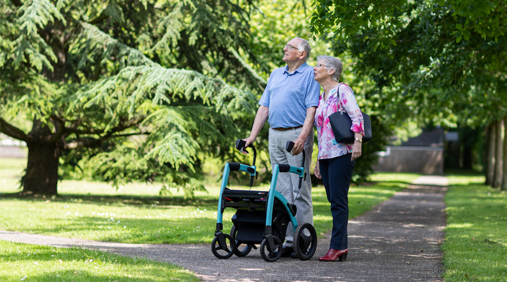 Man with rollator walking in the park with his wife